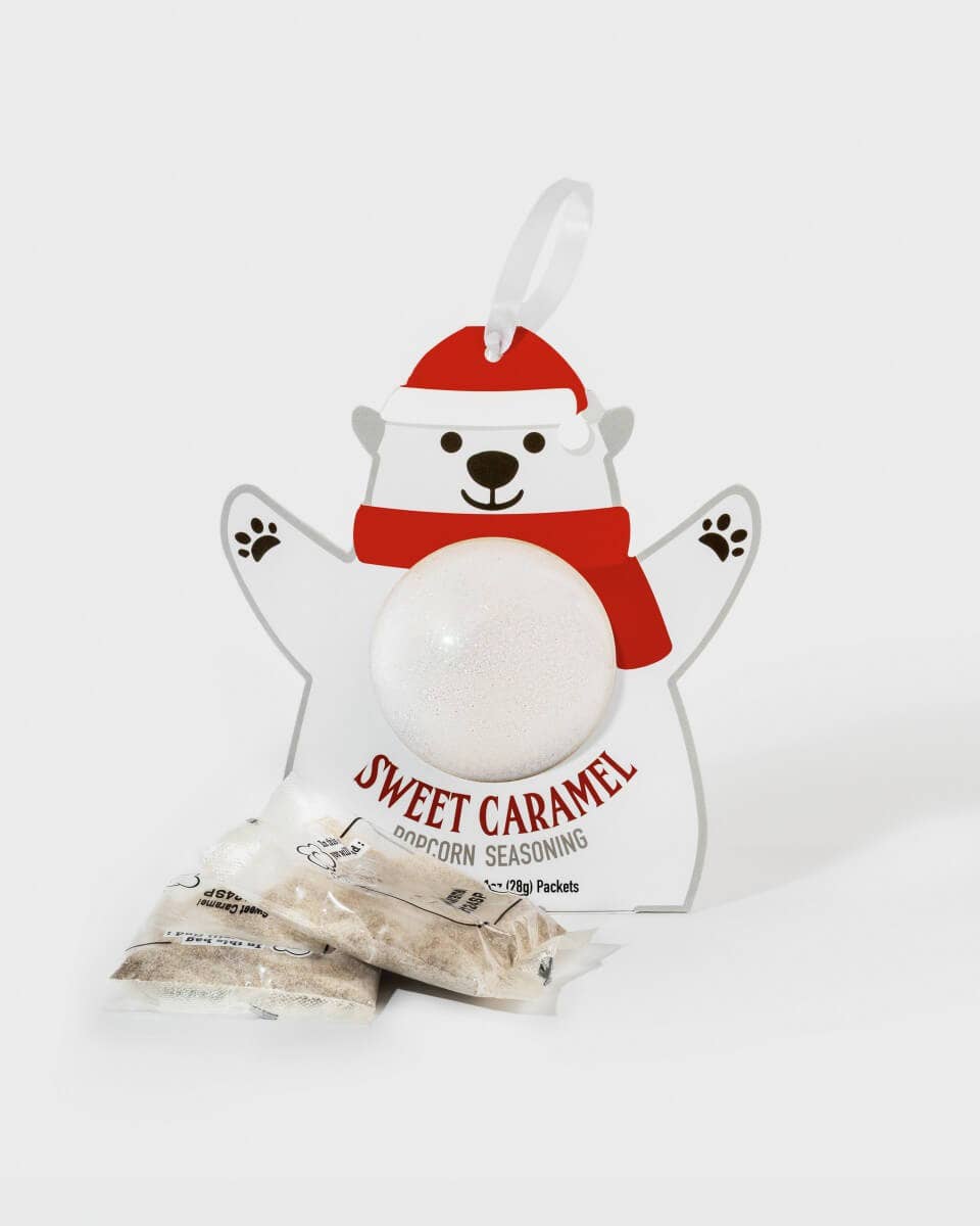 A white bear-shaped package labeled 'Sweet Caramel Corncorn Seasoning' with a red Santa hat and red scarf, shown on a light gray background with two small seasoning packets in front.
