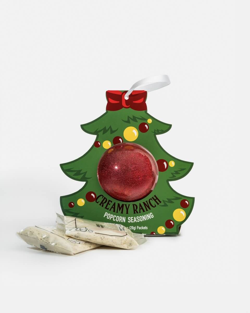 A Christmas tree-shaped Creamy Ranch Popcorn Seasoning box with a red glitter ornament in the center and several seasoning packets placed in front, photographed on a clean white background.