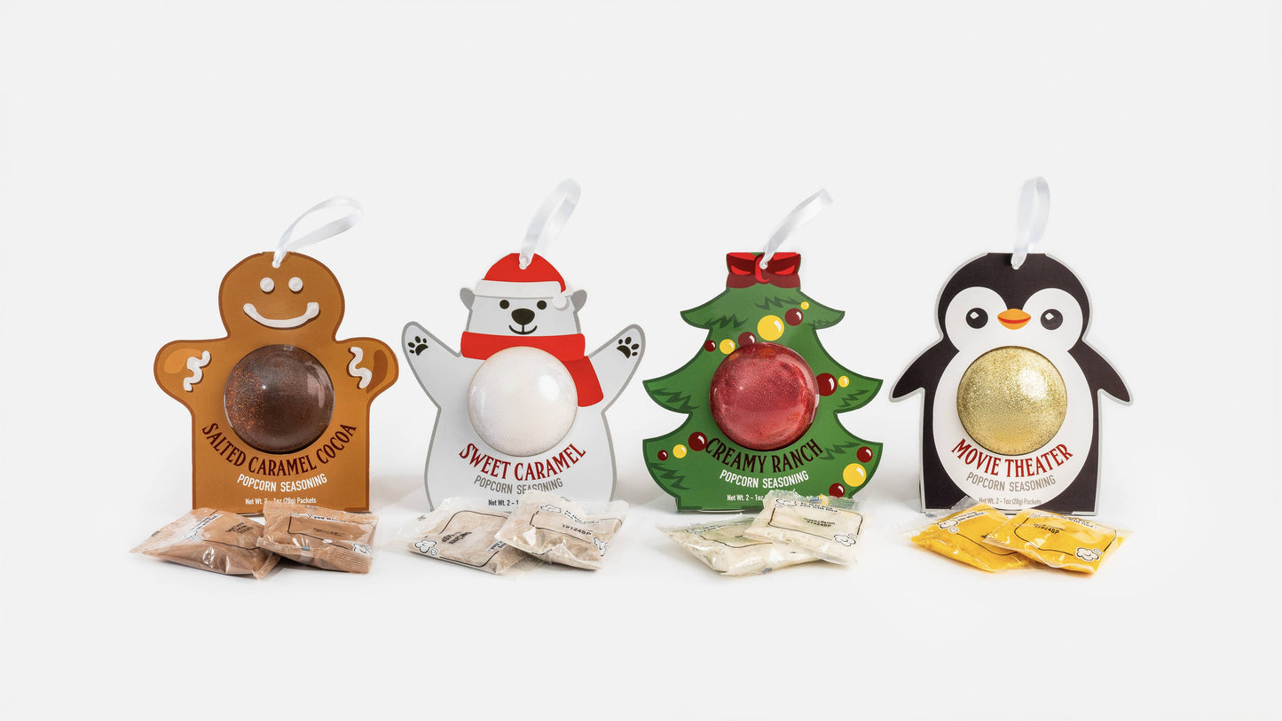 Four Christmas-themed candy gift boxes arranged on a white background: gingerbread man, polar bear, Christmas tree, and penguin, each with a wrapped candy visible and small candy packets in front.