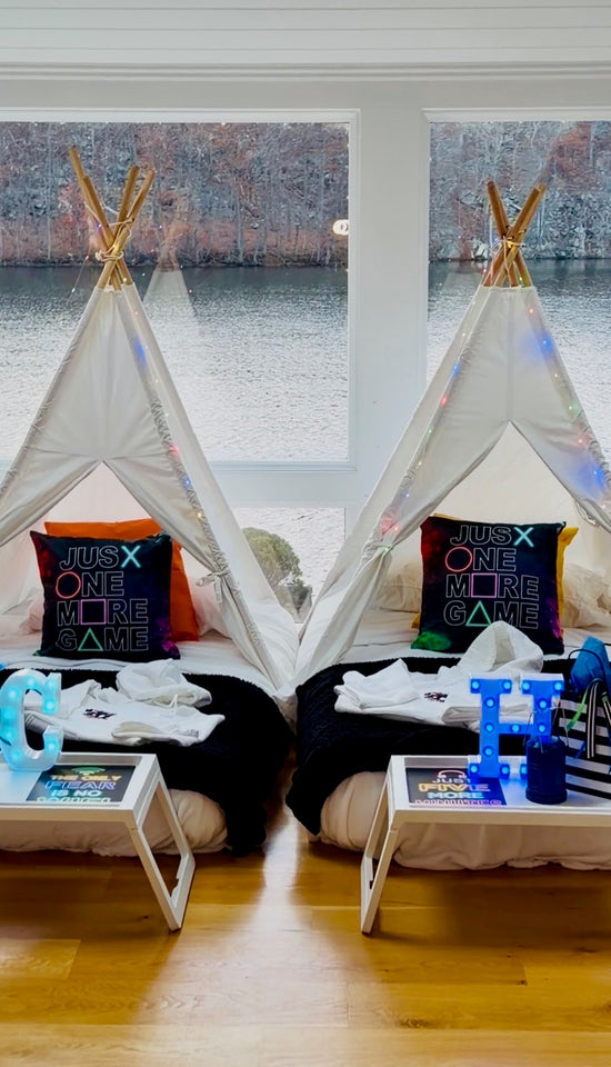 Two children's teepees with pillows and toys in a room with large windows.