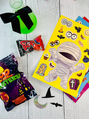 Halloween-themed items including a book with stickers, candy packages, and decorative elements on a wooden surface.
