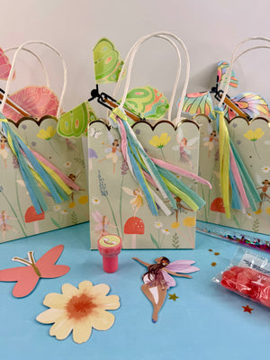 Colorful gift bags with fairy designs and ribbons on a light blue surface.