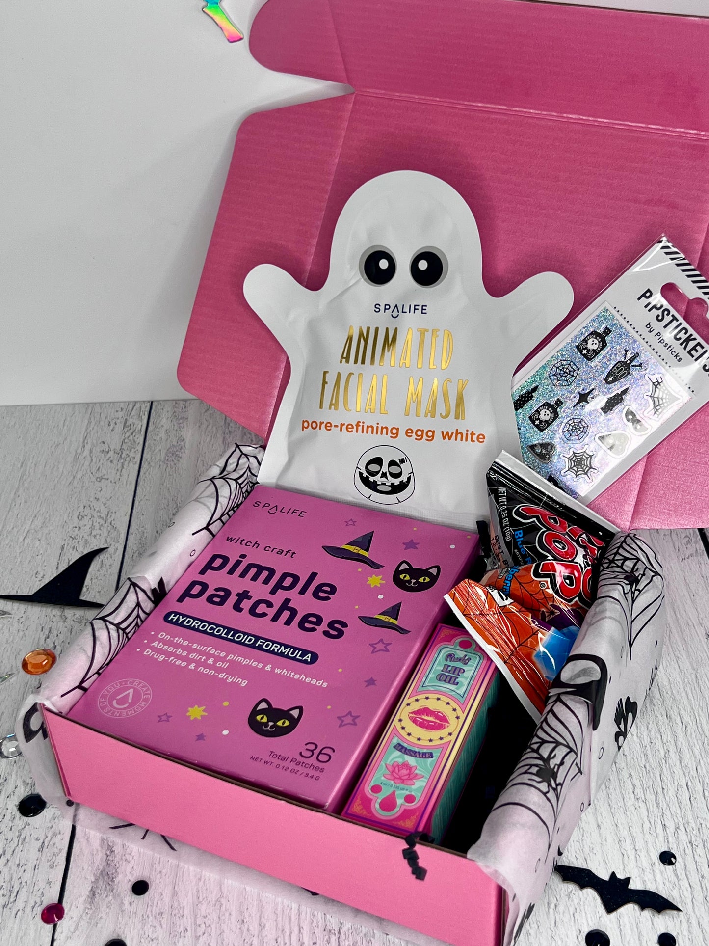 Pink box with skincare products including a ghost-shaped mask and pimple patches on a white background.