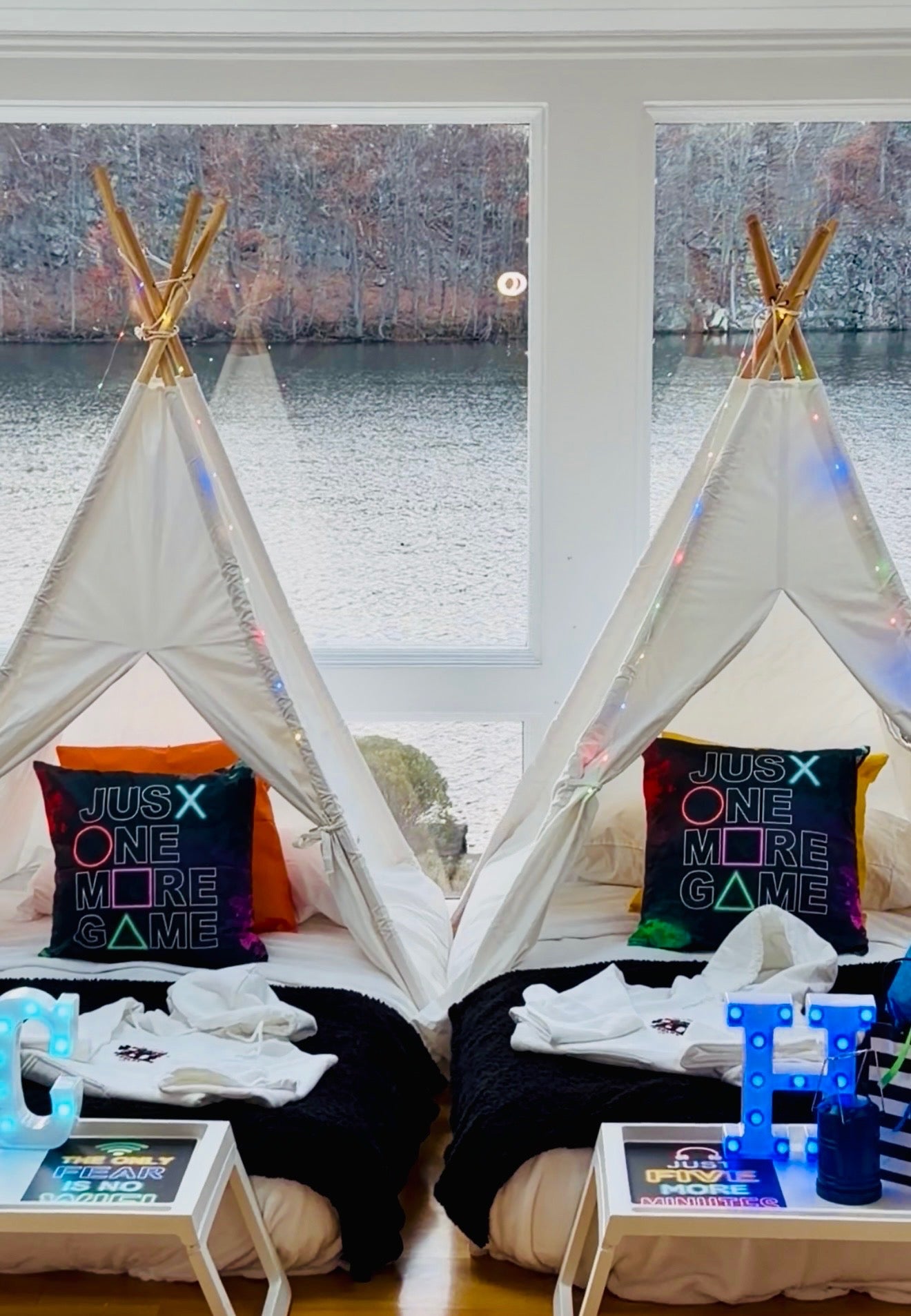 Two children's teepees with pillows and toys in front of a window with a view of water.