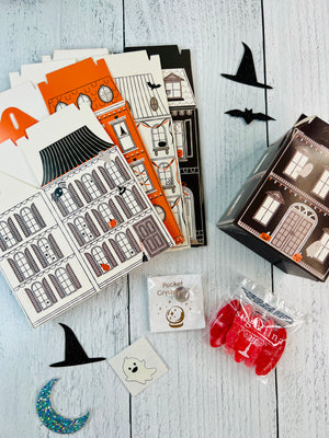 Halloween-themed stationery set with houses, cards, and decorative items on a wooden surface.