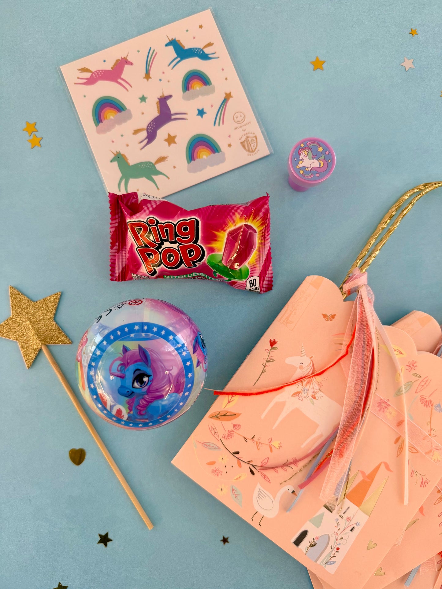 Assorted party favors including a 'Ring Pop' candy, balloons, and a notebook on a blue background.