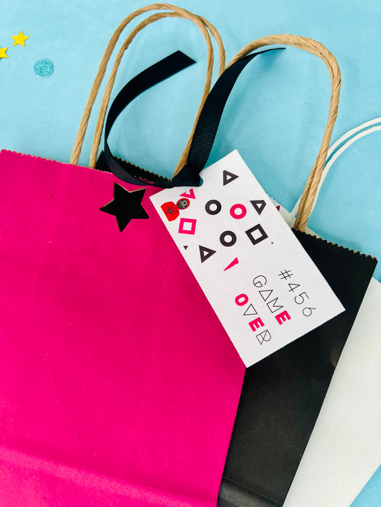 Pink gift bag with a black star, black gift bag with a white tag, and a blue background.