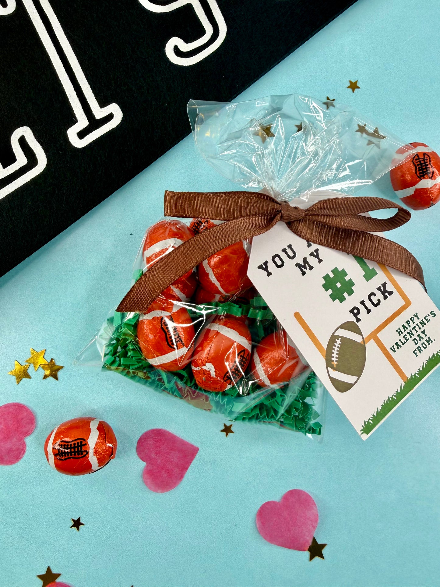 Candy footballs in a clear bag with a brown ribbon and 'You're My Pick' tag on a light blue background.