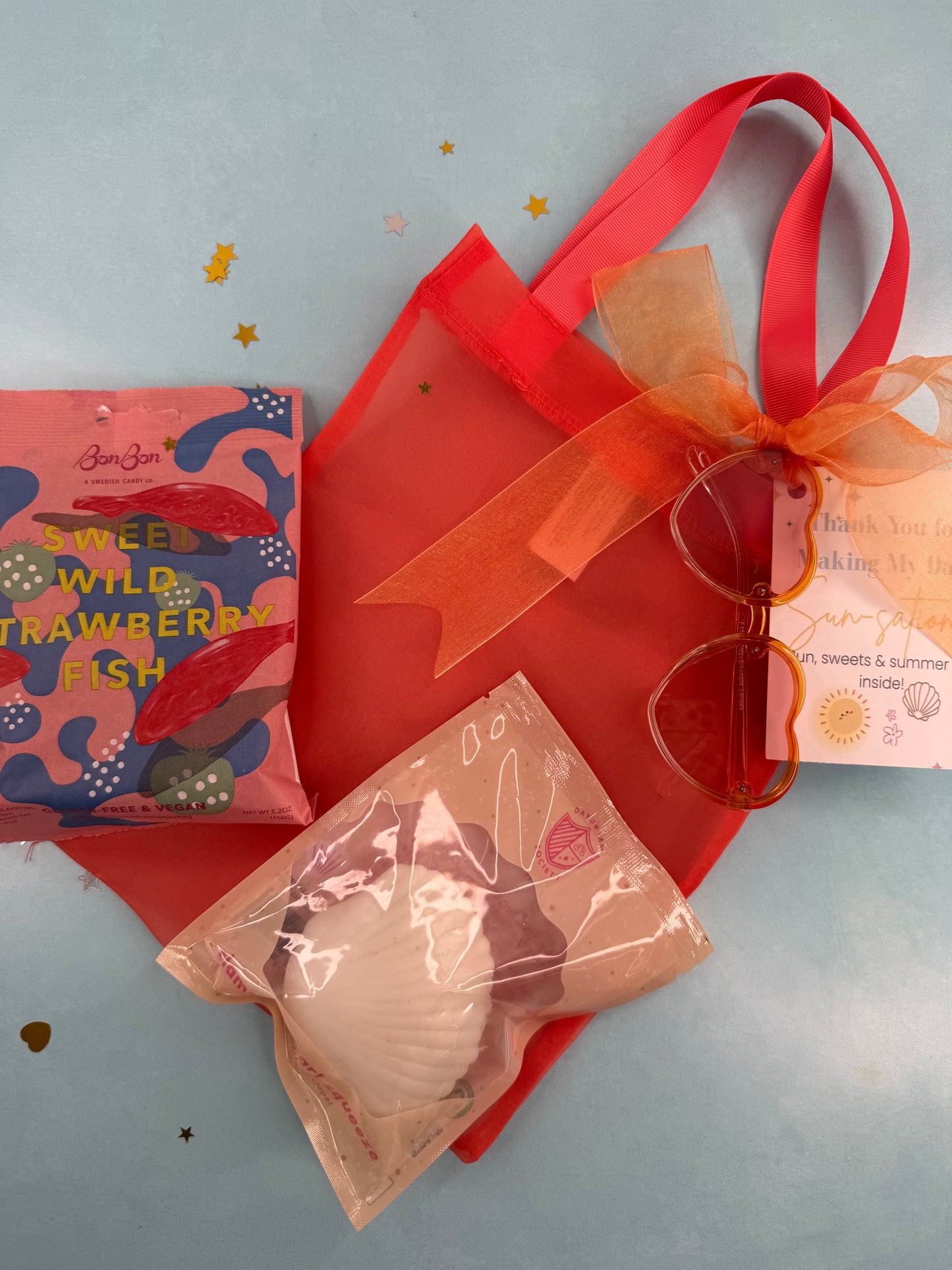Red gift bag with orange ribbon, sunglasses, and a small item on a light blue background