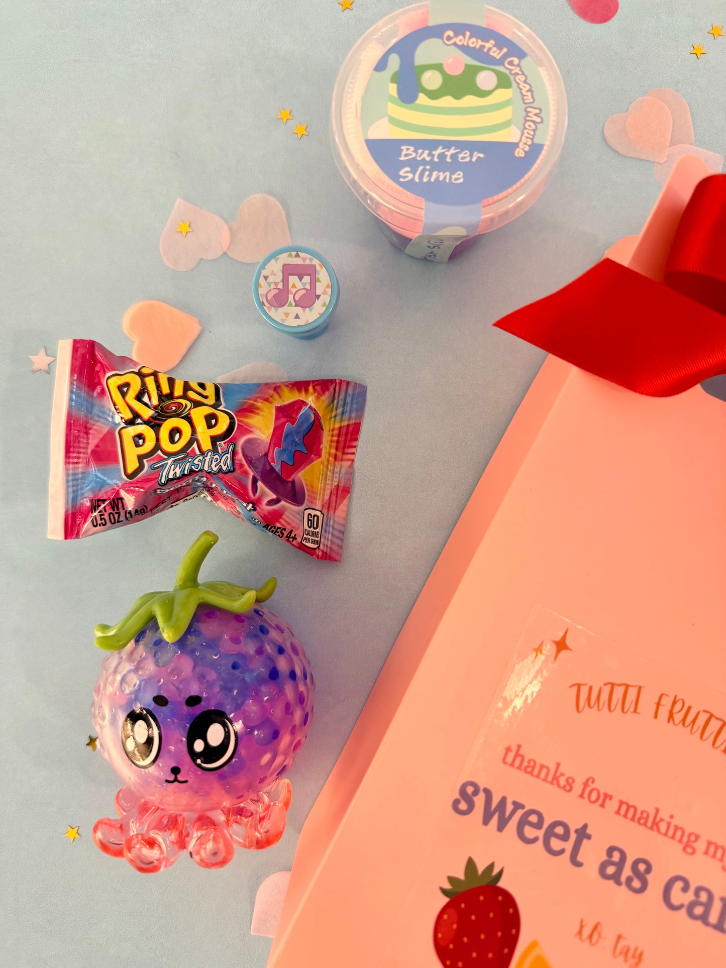 Colorful toy octopus, Rody Pop Twirled candy, and containers of slime on a light gray background.