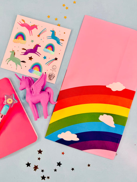Colorful stationery items including a pink unicorn figurine, rainbow notebook, and star-shaped stickers on a light blue background.