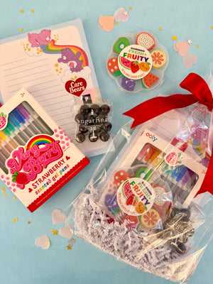 Assorted stationery items including a notebook, pens, and gummy bears on a light blue background.