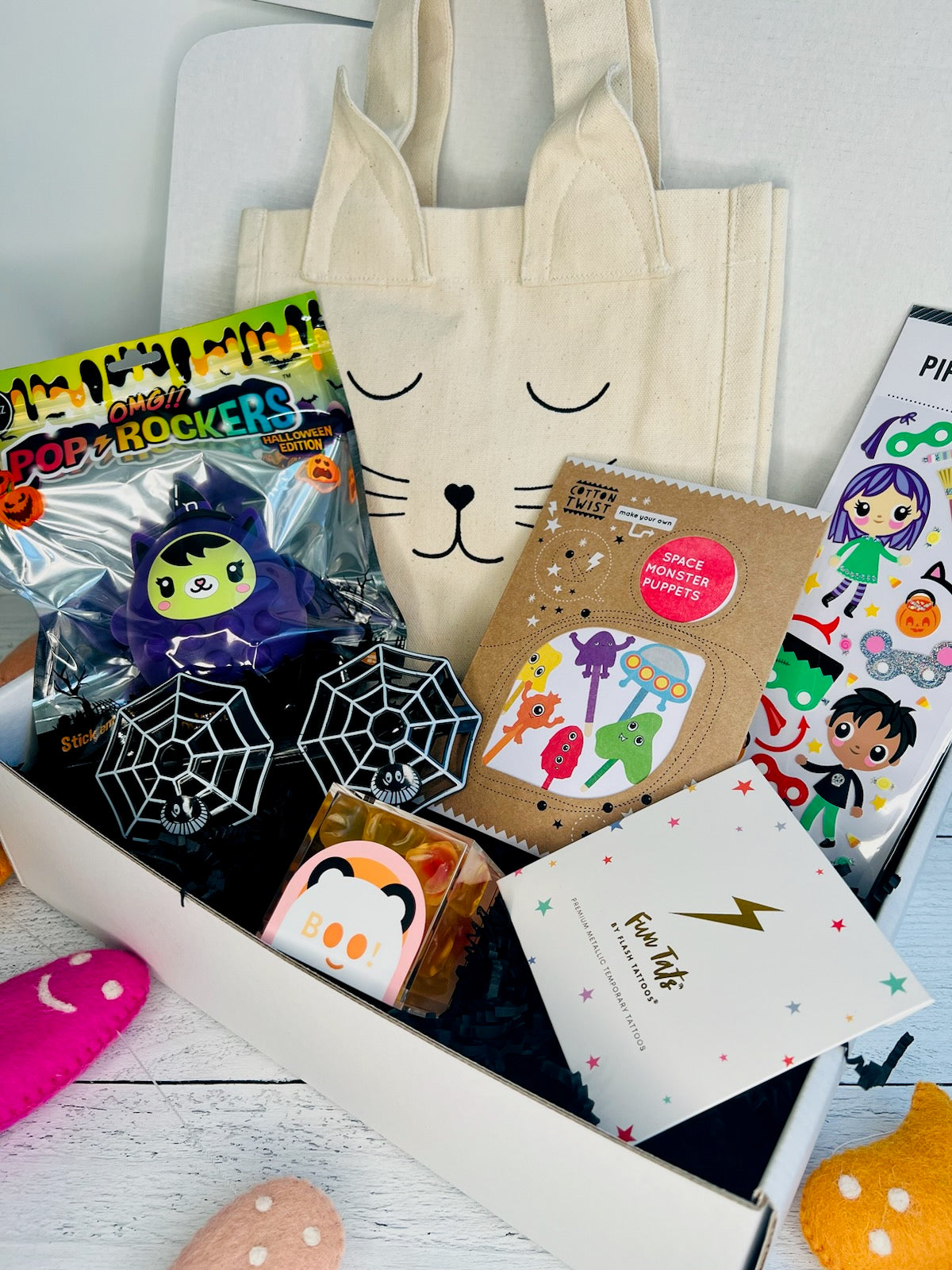 A collection of Halloween themed items including a cat-shaped tote bag, puppet theater, temporary tattoos, and other small toys arranged in an open box.