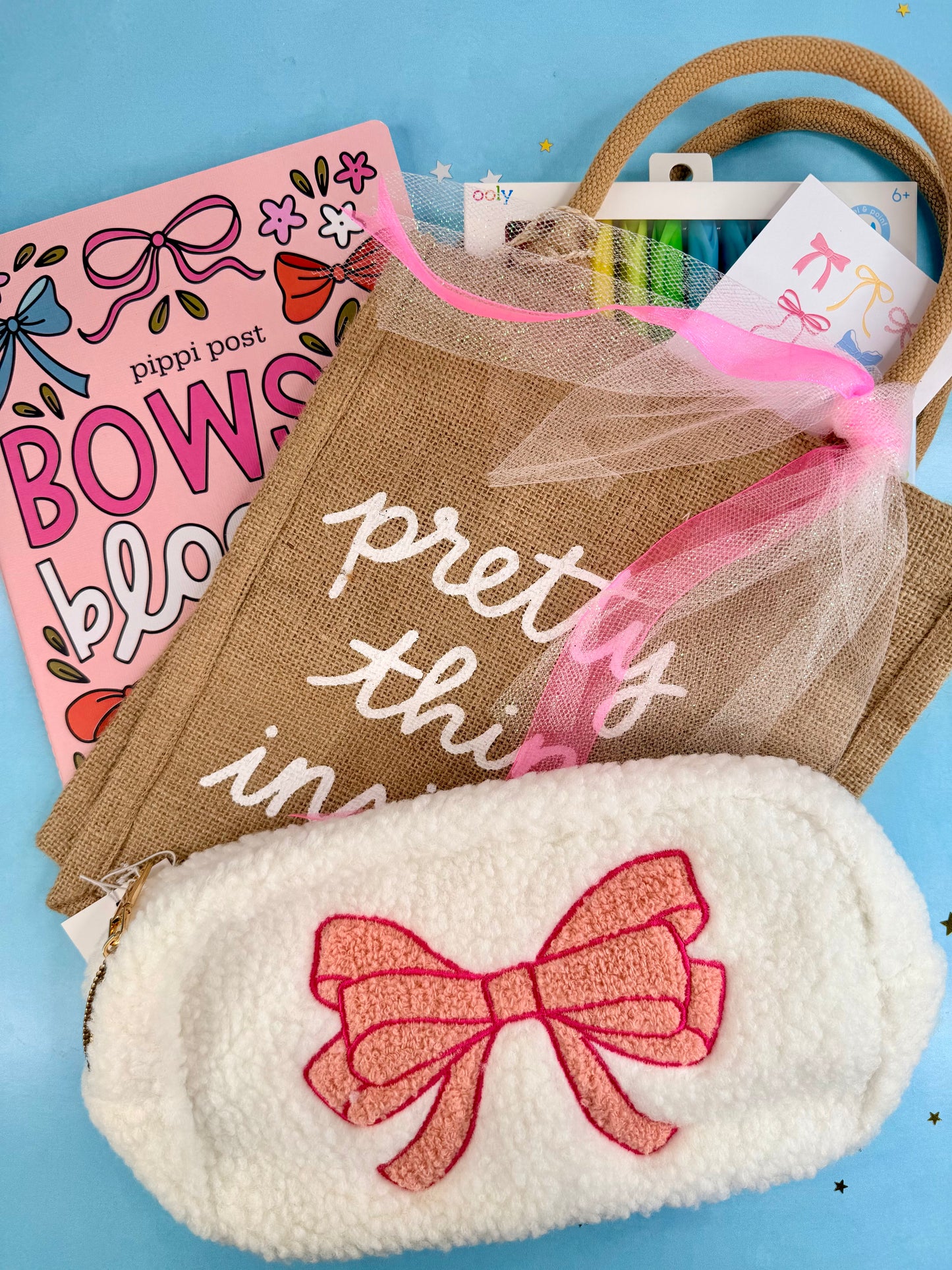 White eye mask with pink bow, burlap bag with text, and pink book on blue background