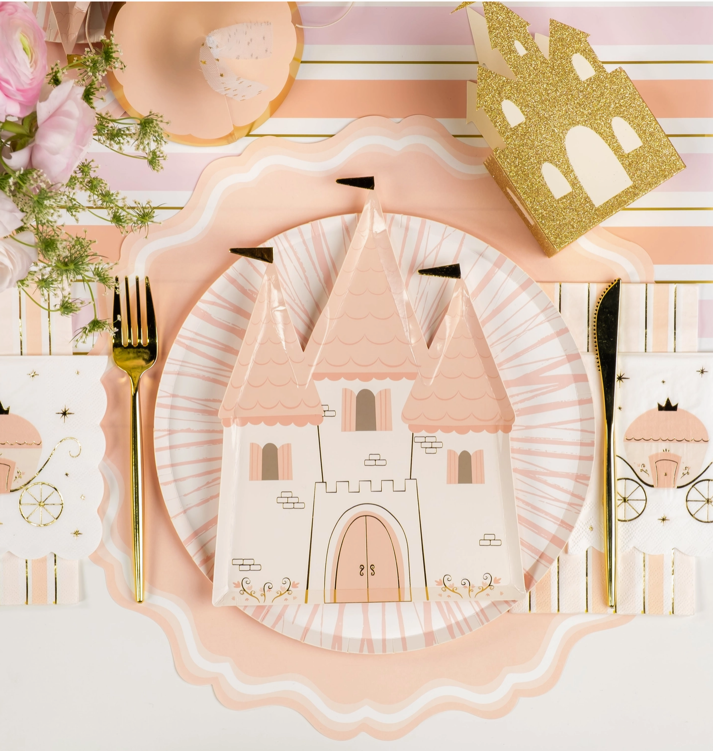 Table setting with castle-themed plates, gold cutlery, and decorative items on a pink and white background.