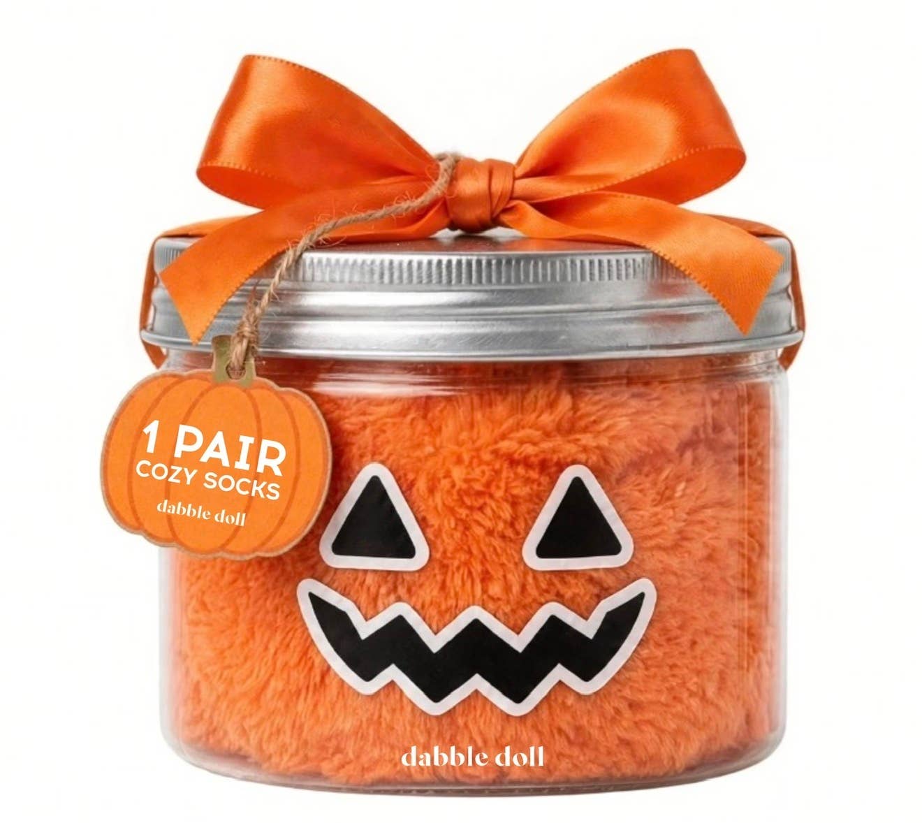 An orange fluffy pair of cozy socks packaged in a clear jar with a silver lid, decorated with an orange ribbon bow and a pumpkin-shaped tag that reads '1 PAIR COZY SOCKS dabble doll'.