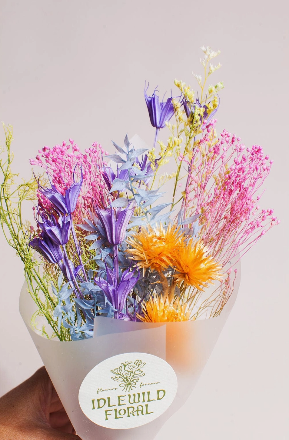 Bouquet of colorful flowers in a white container with 'Idlewild Floral' label on a light gray background
