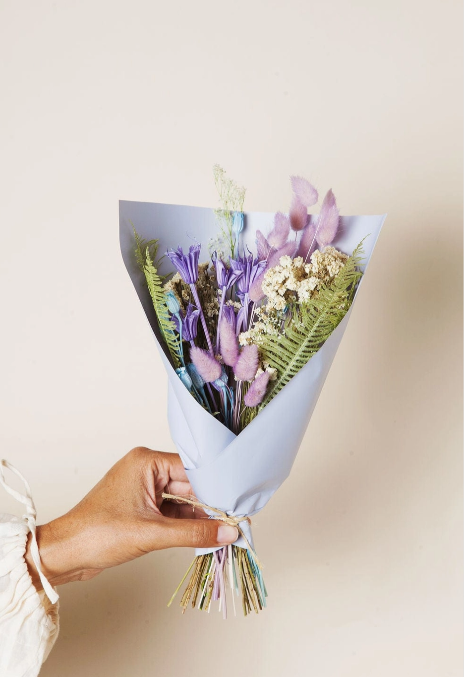 Bouquet of flowers wrapped in paper held by a hand on a light background