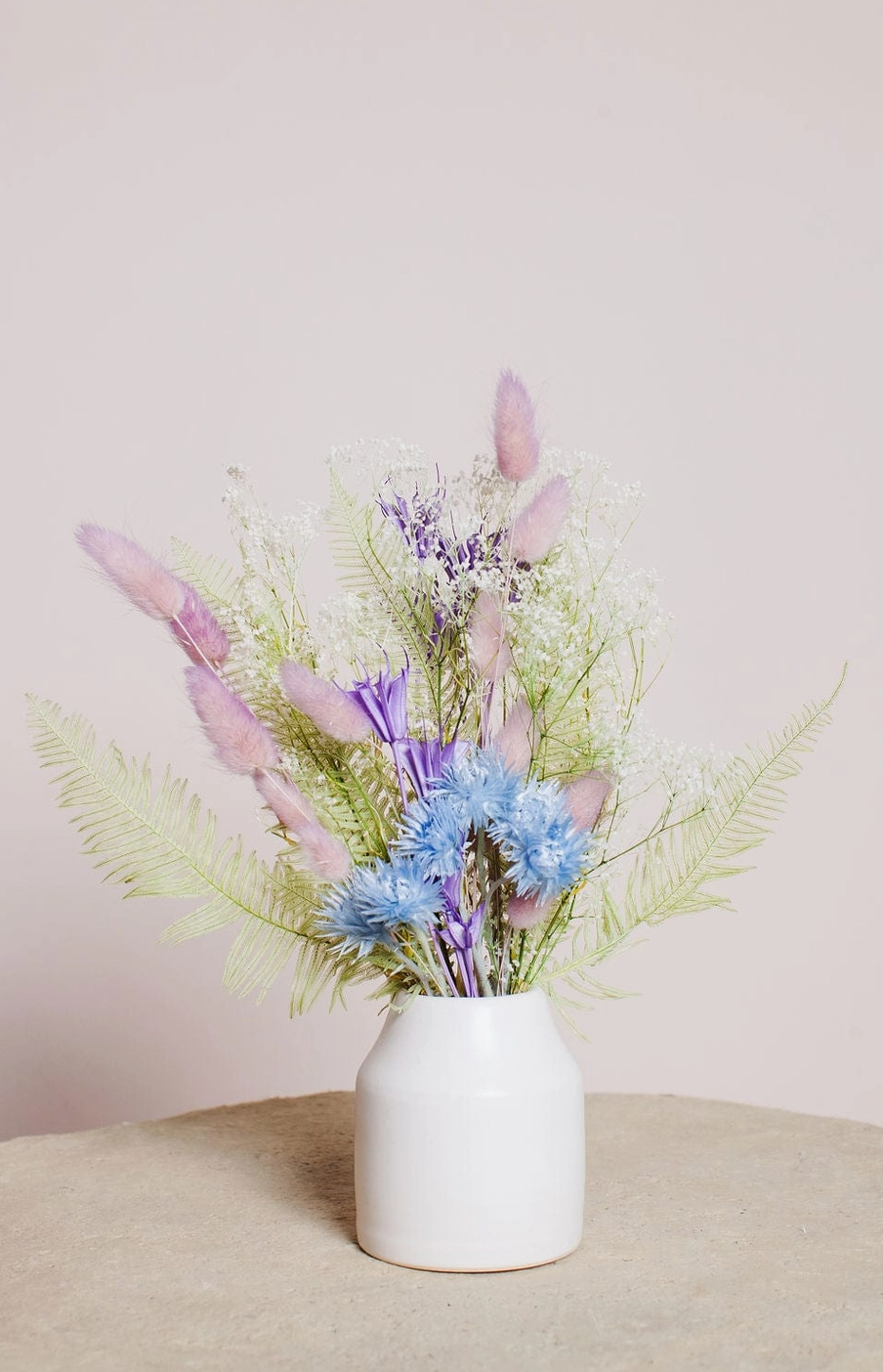 White vase with dried flowers on a beige surface and light pink background