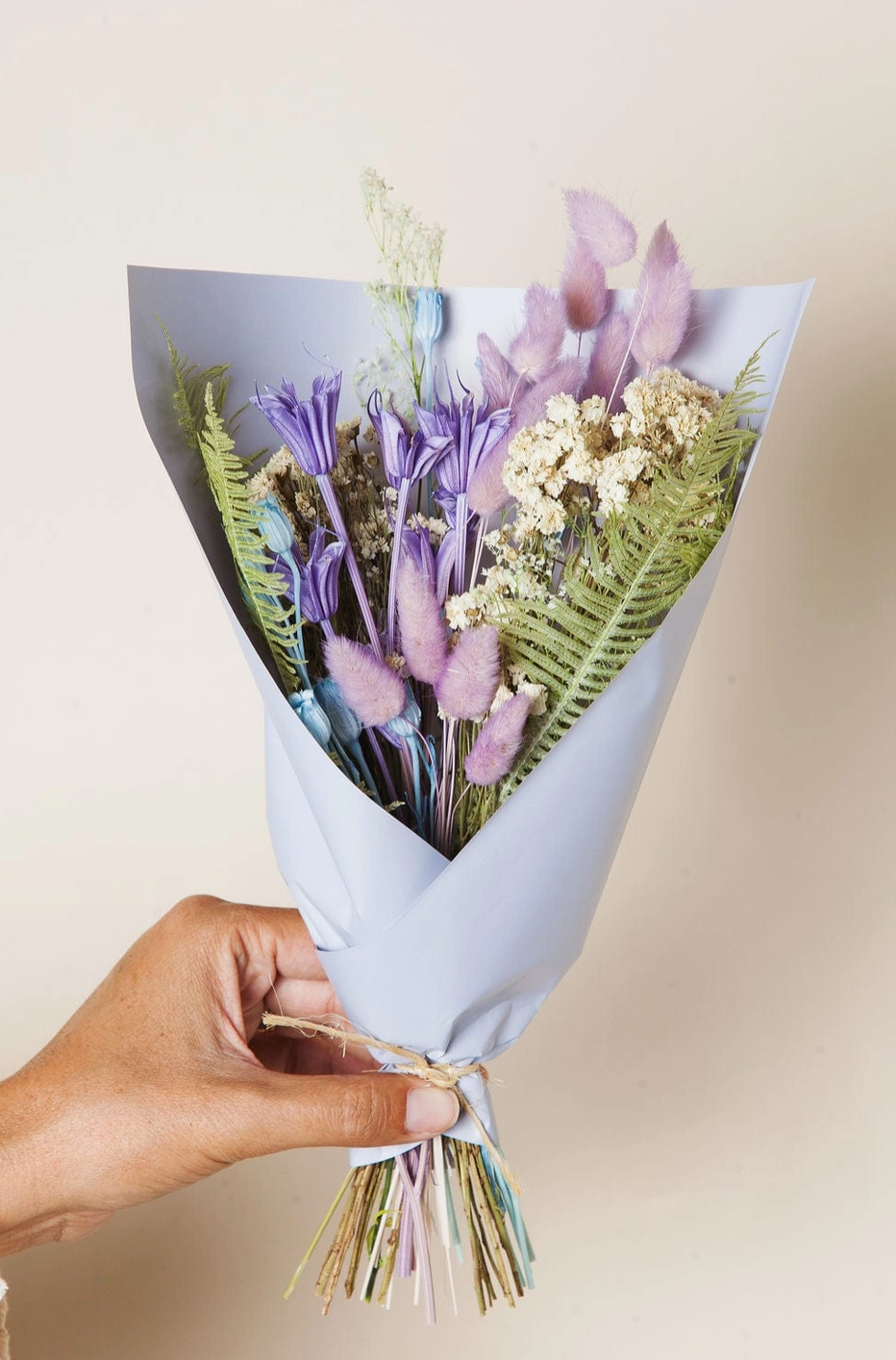 Bouquet of flowers wrapped in paper held by a hand against a plain background