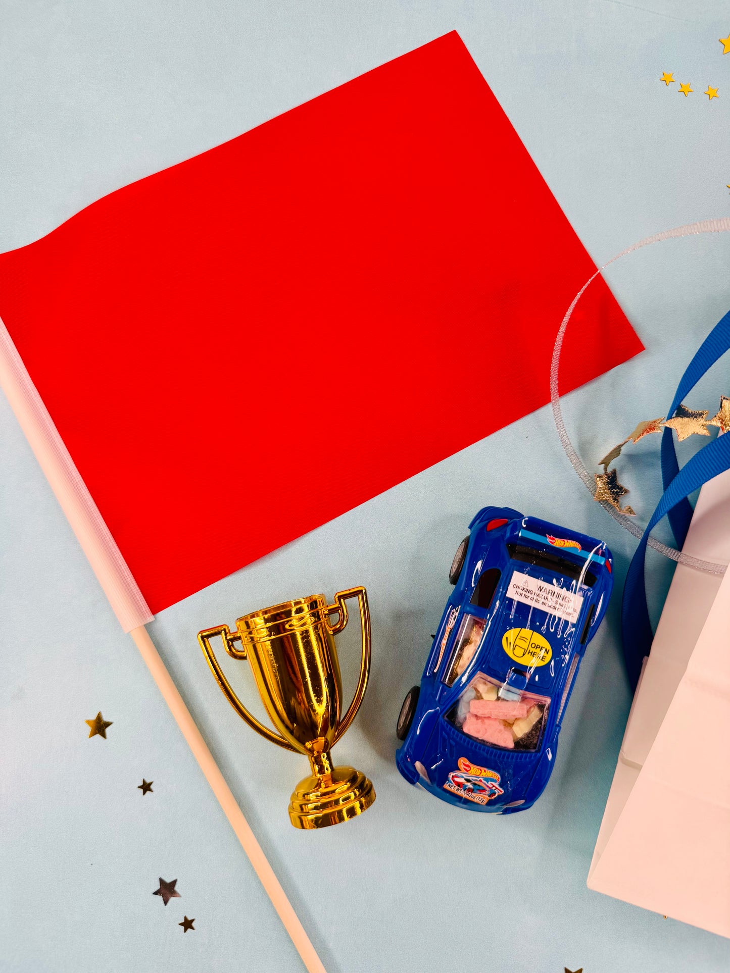 Toy car, gold trophy, and red paper on a light blue background