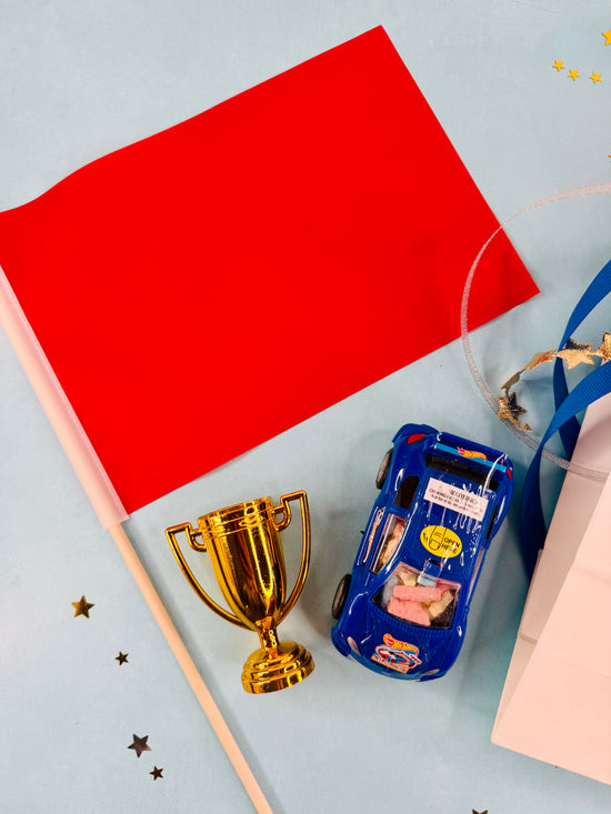 Toy car, gold trophy, and red paper on a light blue background
