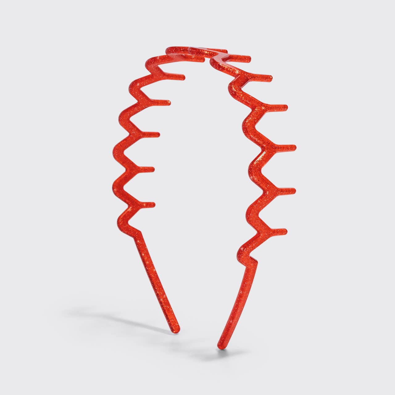 A red glittery metal zigzag headband on a light gray background.