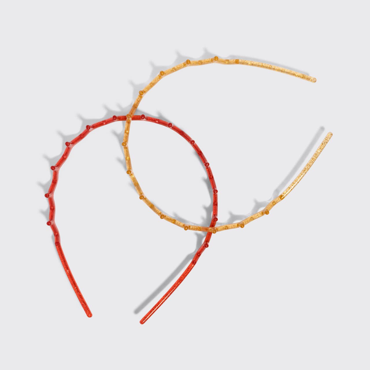 Two thin headbands with small bead details, one in red and one in gold, arranged on a light gray background.