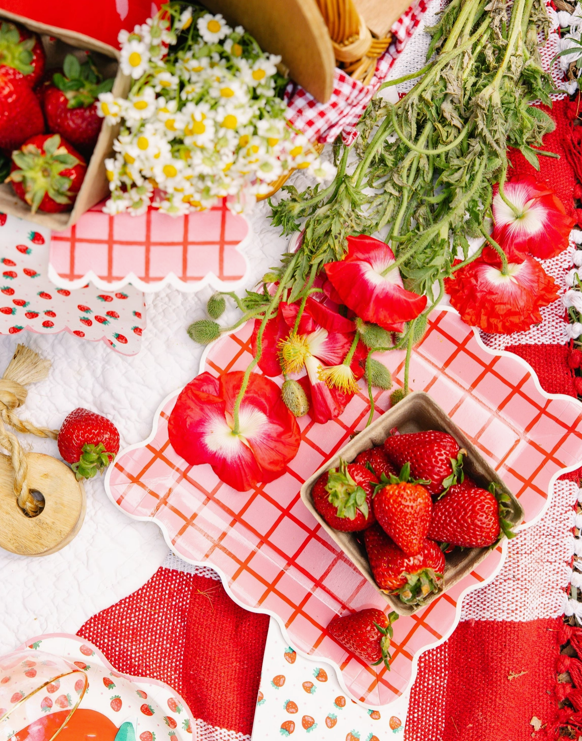 Strawberries and flowers on a red checkered tablecloth with a decorative plate.