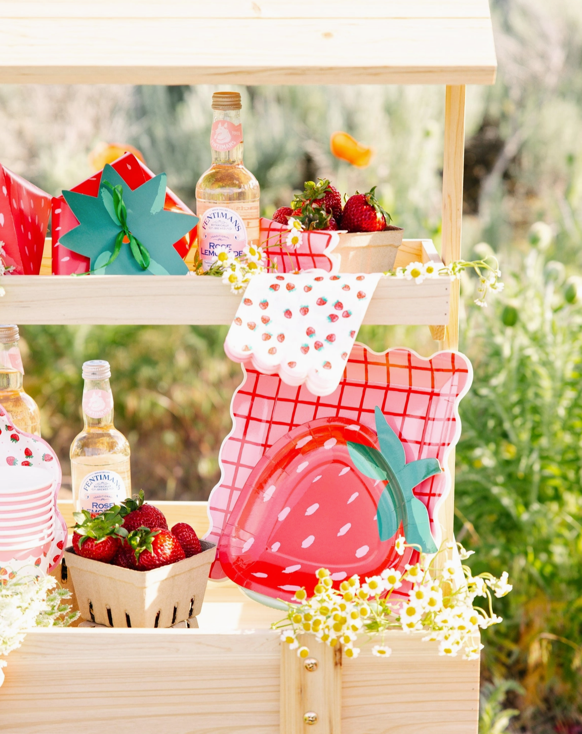 Outdoor setting with strawberry-themed decor, bottles, and a wooden cart.