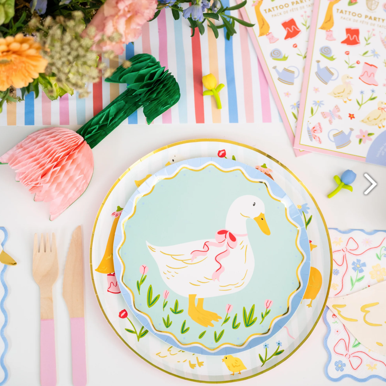 Colorful party table setting with a duck-themed plate, flowers, and party supplies.