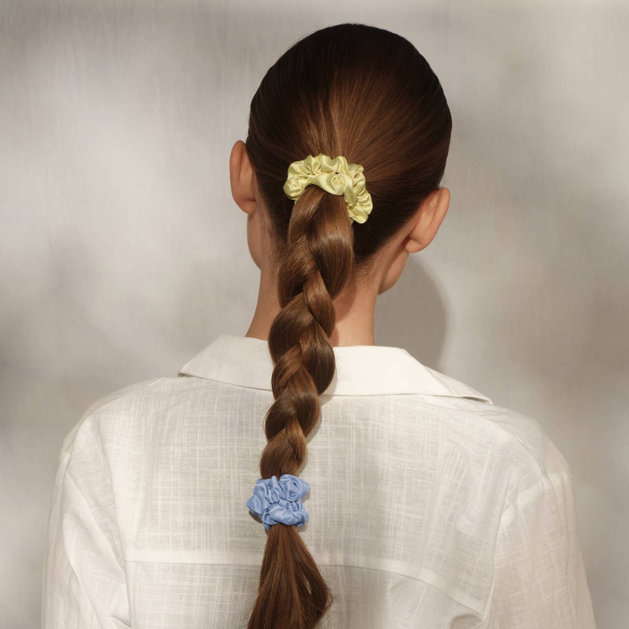 Person with braided hair using colorful scrunchies on a plain background