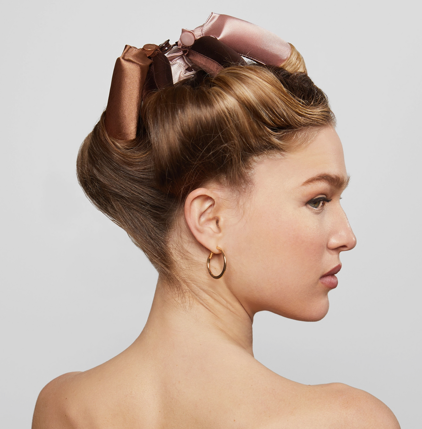 Woman with styled hair featuring a large pink bow on a plain background