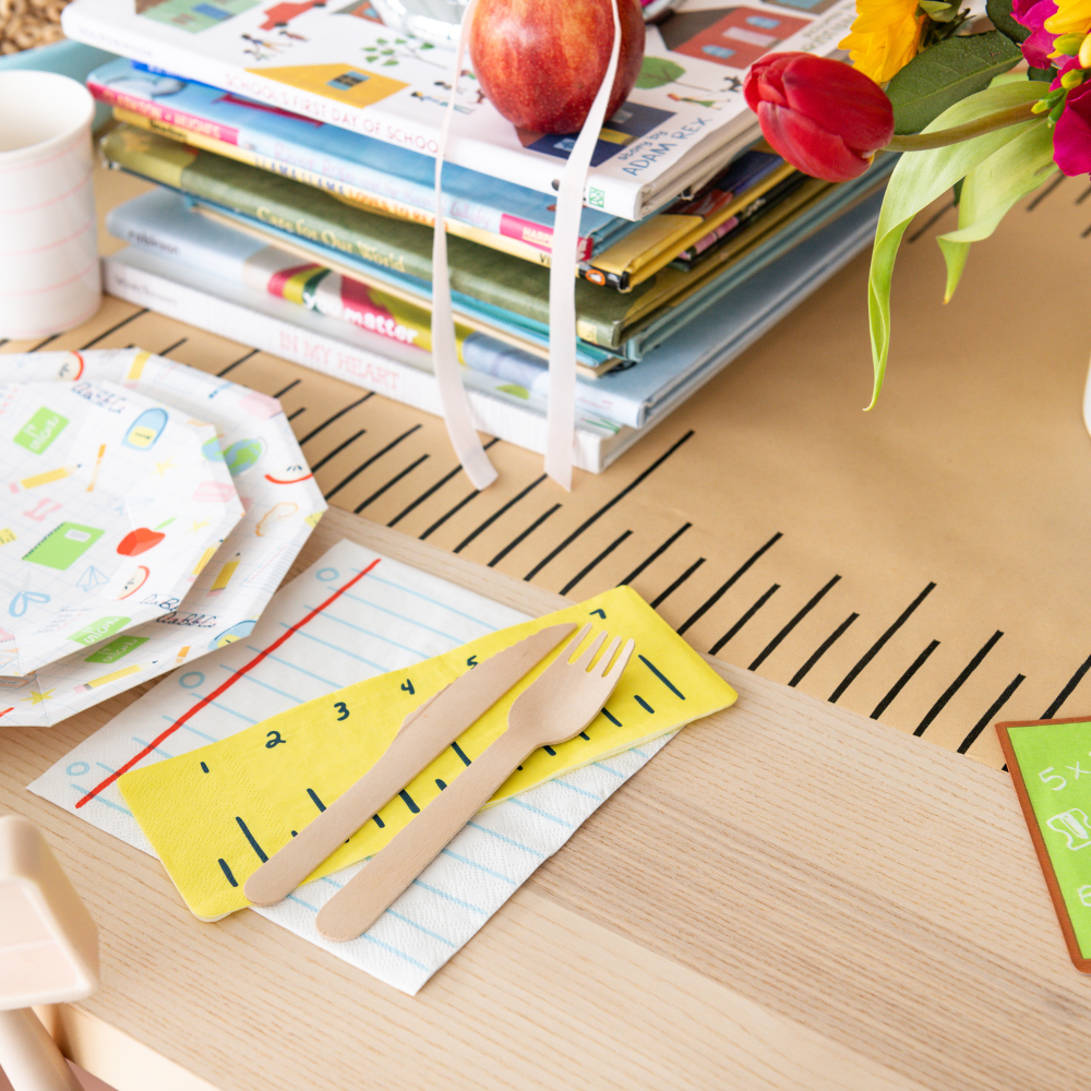 Children's table setting with books, cutlery, and a mug on a wooden surface.