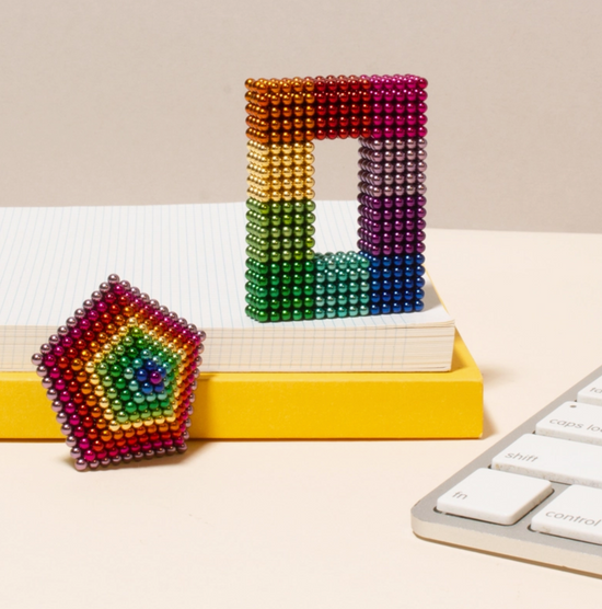 Colorful magnetic bead structures on a desk with a keyboard and books in the background.