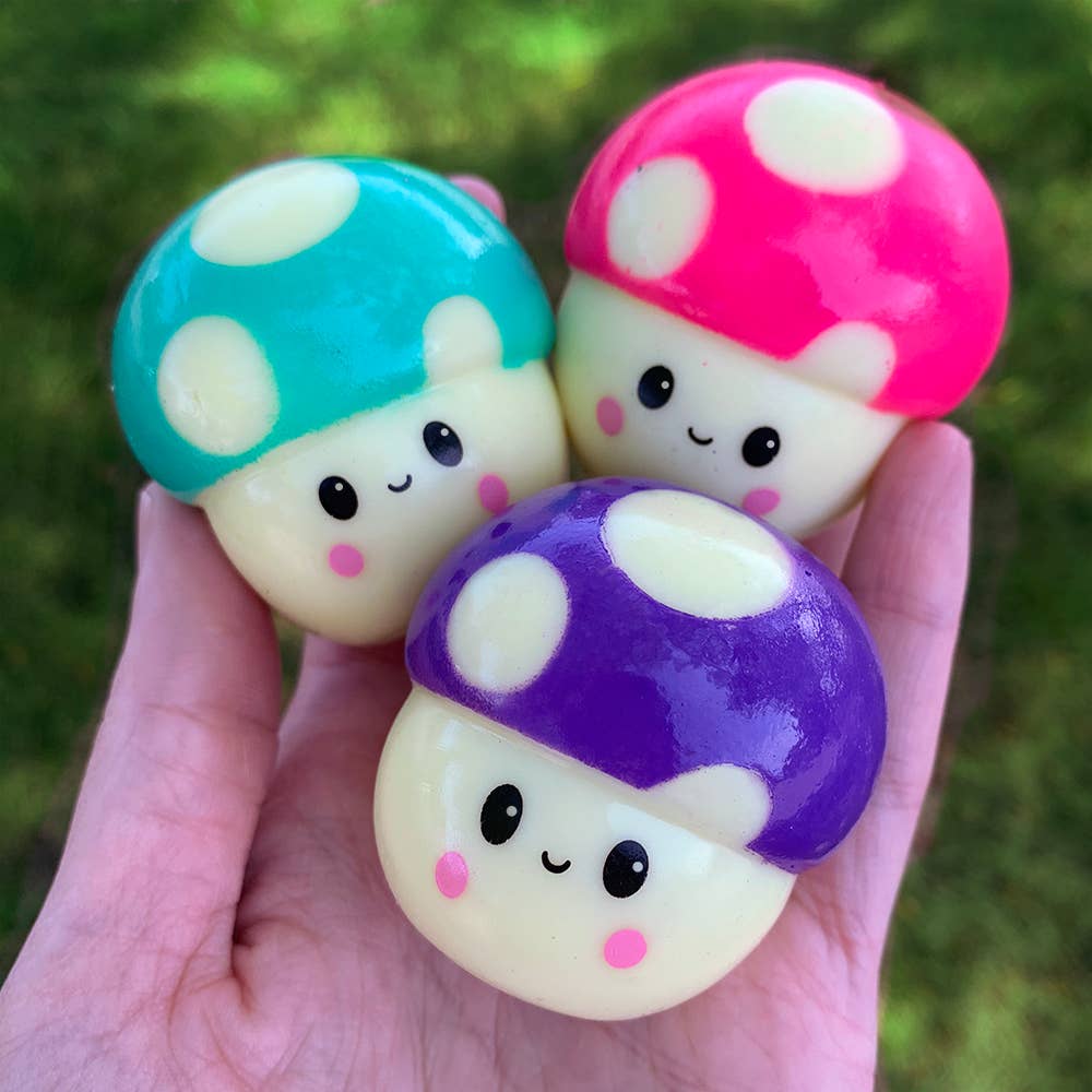 Three colorful mushroom-shaped squishies held in a hand with a green blurred background
