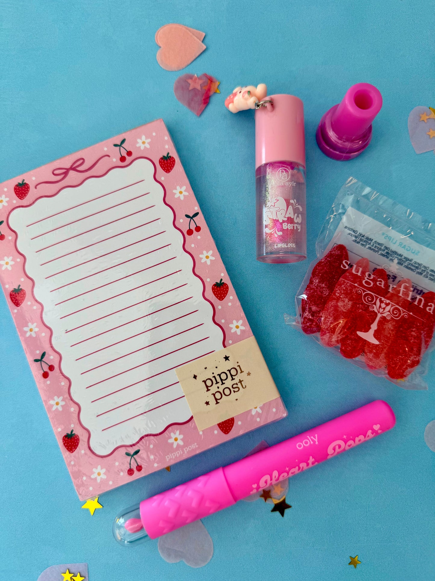 Pink stationery set with a notepad, pen, and small items on a blue background