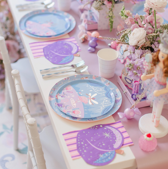 Children's table setting with pastel-colored plates, napkins, and decorations on a pink tablecloth.