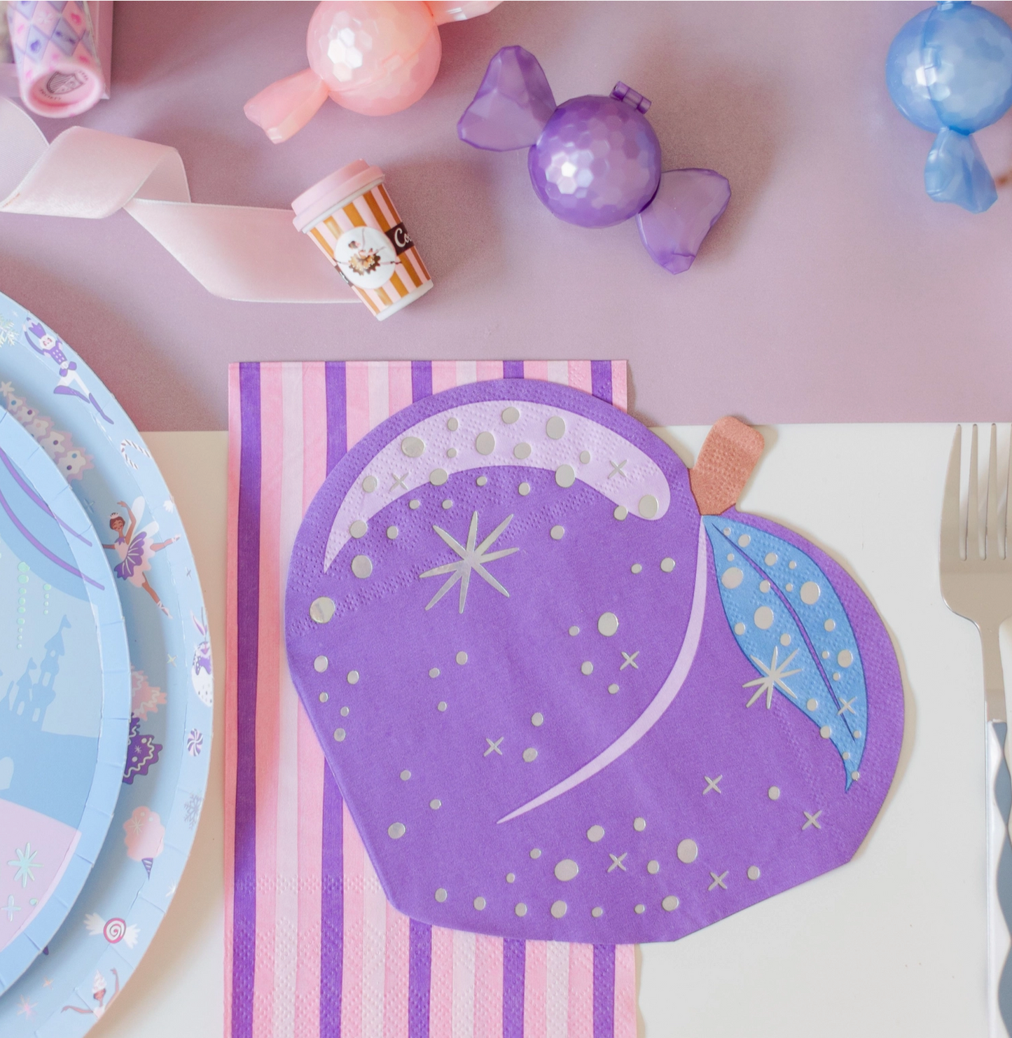 Purple fairy-themed paper plate with decorative elements on a pink surface with candy and plates.