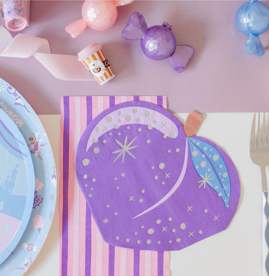 Purple fairy-themed paper plate with decorative elements on a pink surface with candy and plates.