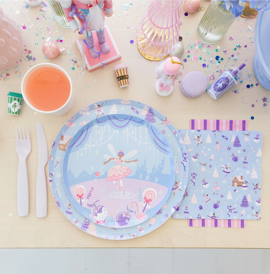 Fairy-themed tableware including plates, cutlery, and napkins on a light surface with colorful decorations.