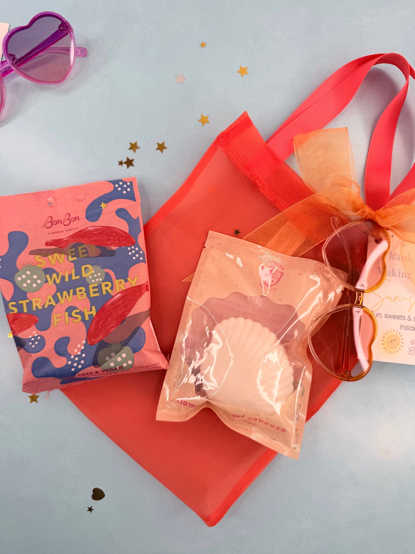 Sunglasses with orange ribbon, pink packaging, and heart-shaped object on light blue background