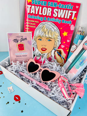 A gift box containing Taylor Swift themed items including a coloring and activity book, heart-shaped sunglasses, a black gel ink pen, lip balm, coloring pencils, and a woven bracelet.