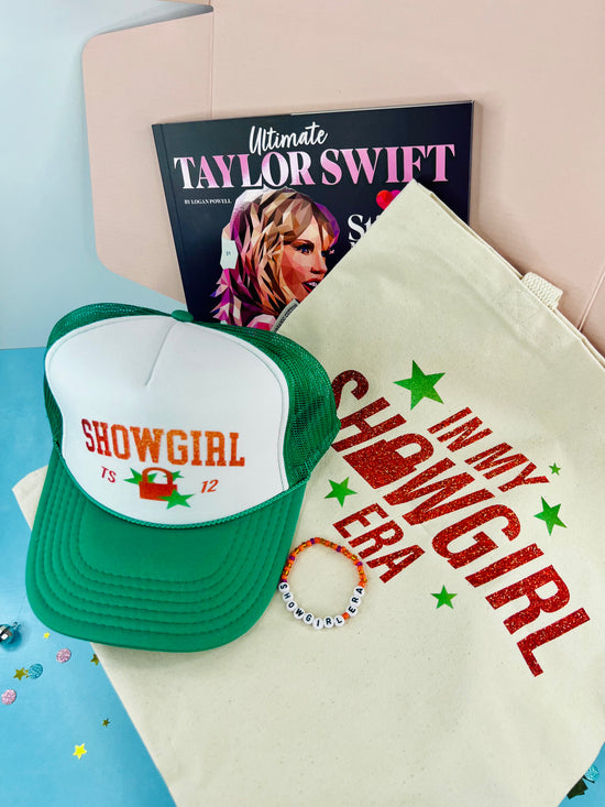 Green and white cap with 'Showgirl' text, t-shirt with similar design, and magazine in the background