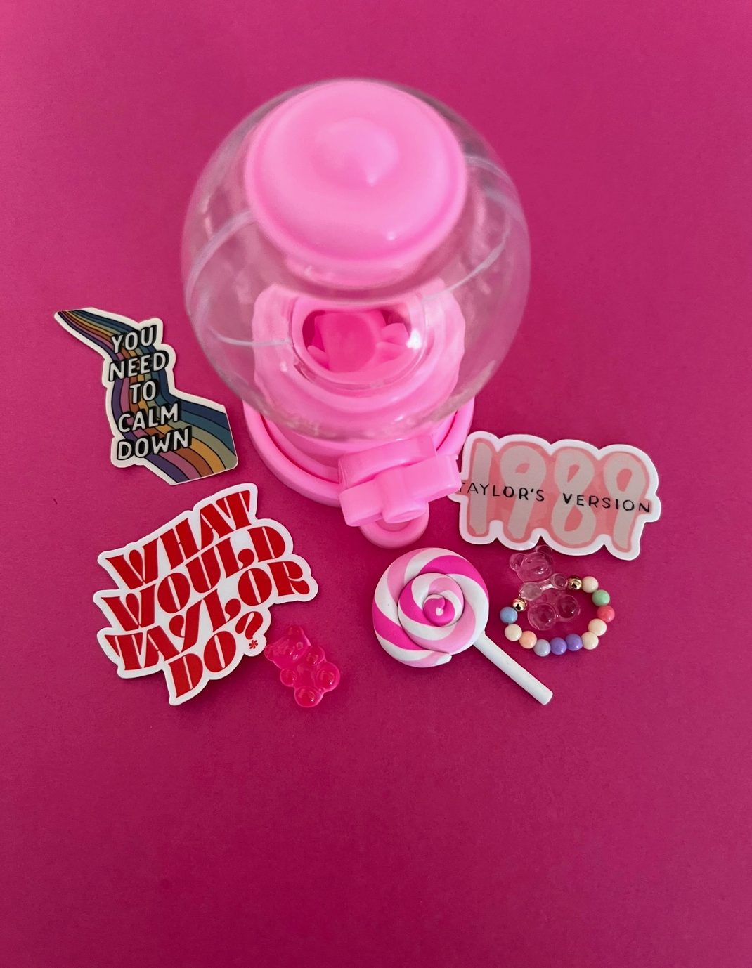 A collection of items including a pink bubble gum machine, various stickers with phrases, a mini plastic lollipop, and plastic gummy bears.