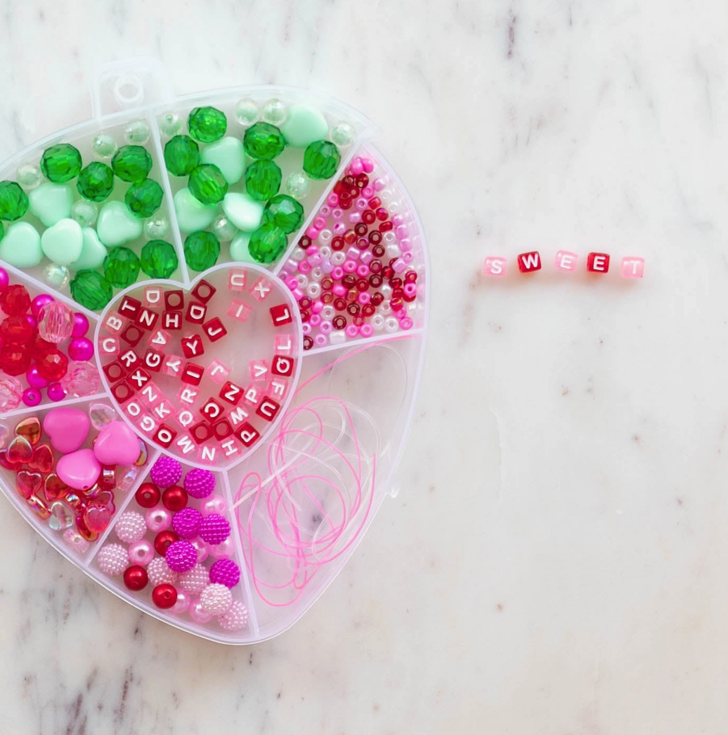 Heart-shaped container with colorful beads and letter beads on a marble surface.