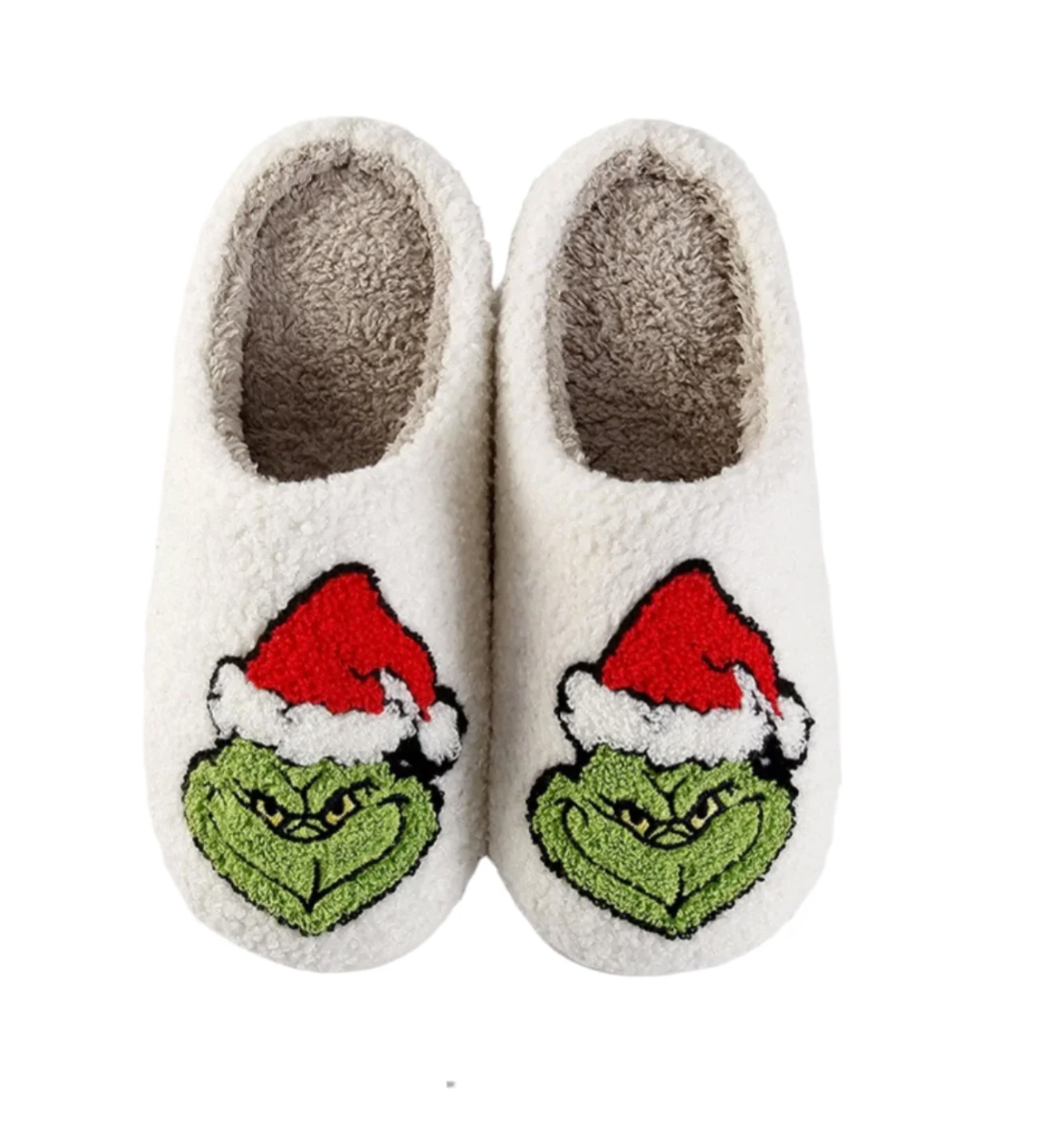 Pair of white slippers with Grinch face design on a white background