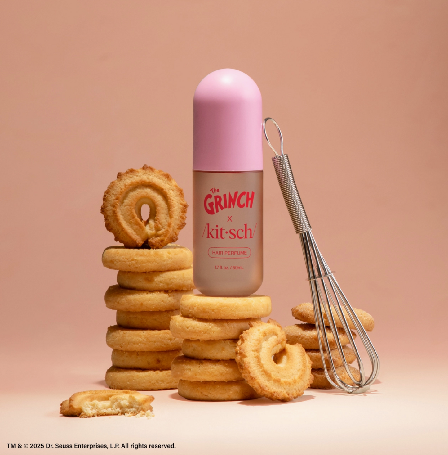 Pink bottle with 'Grinch' branding surrounded by cookies and a whisk on a pink background