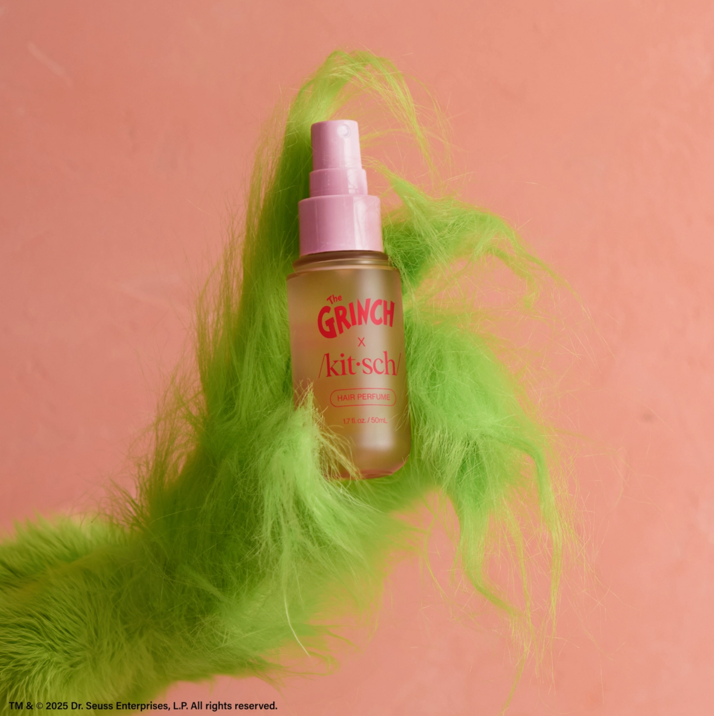 Bottle of 'The Grinch & Kitsch' product with green feathers on a pink background