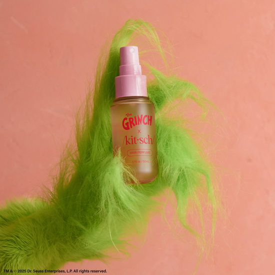Bottle of 'The Grinch & Kitsch' product with green feathers on a pink background